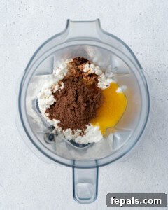 Ingredients inside a blender before mixing: cottage cheese, cocoa powder, and sweetener.