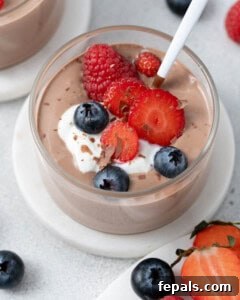Close up of mousse in a glass cup with a spoon, topped with berries and set on a small white plate.