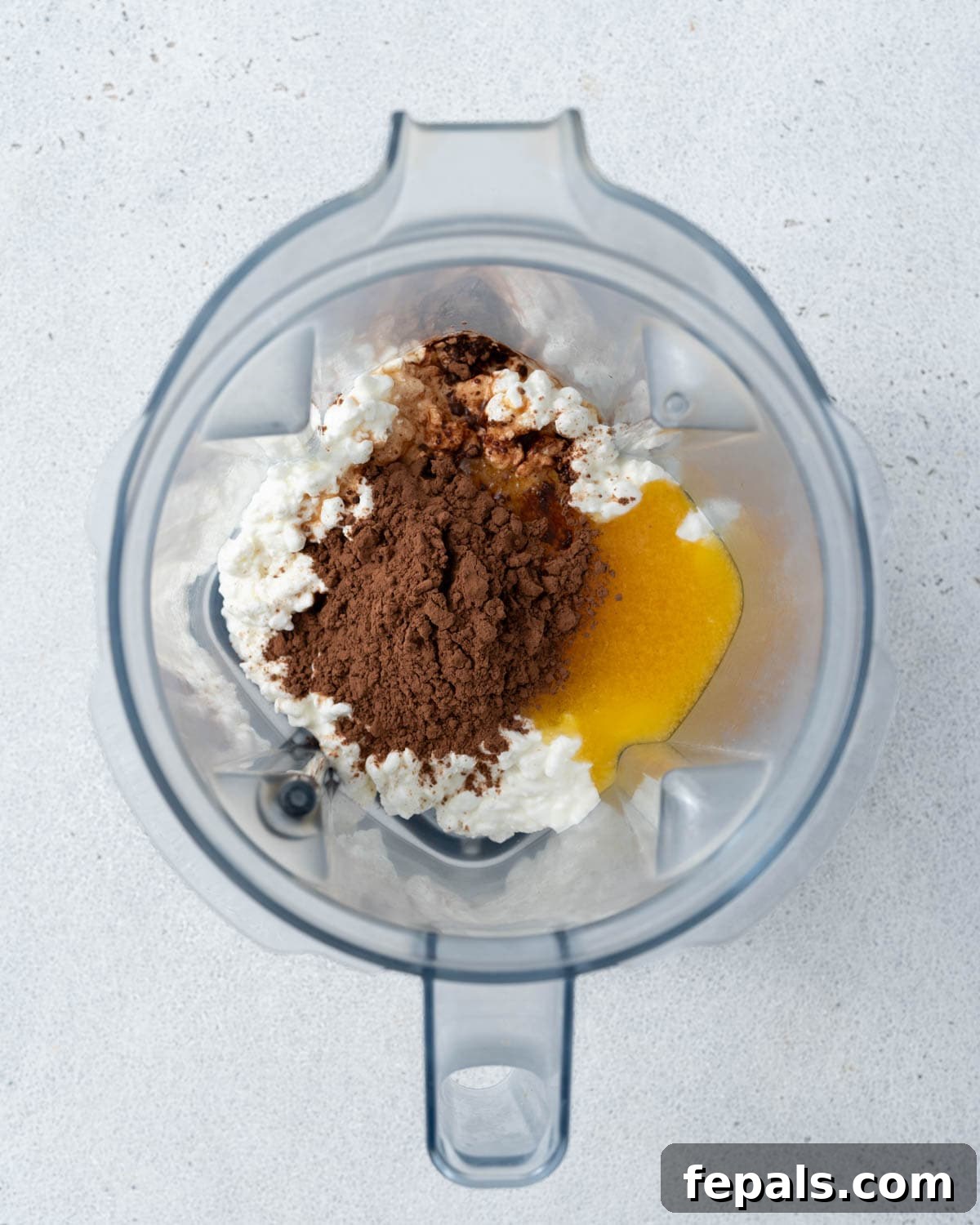 Ingredients inside a blender before mixing: cottage cheese, cocoa powder, and sweetener.