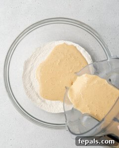 Liquid yogurt mixture being poured over the dry flour mixture in a bowl.