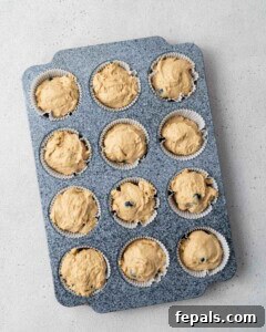 Muffin batter being scooped into a muffin tin pan with liners.