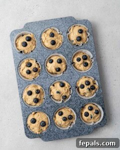 Extra blueberries sprinkled on top of muffin batter in a muffin tin pan before baking.