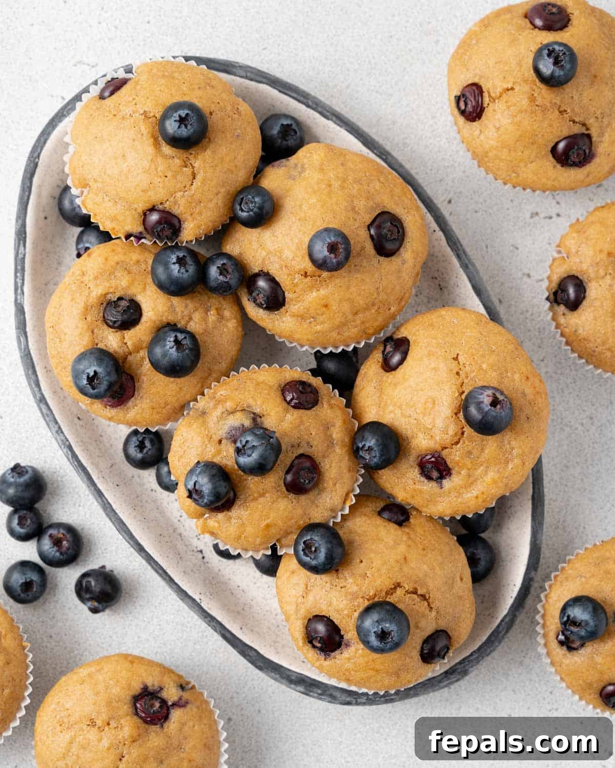 A close-up shot of six beautifully baked blueberry muffins with golden tops and visible blueberries, arranged on a rustic dish.