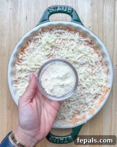 Crustless Pizza Cottage Bowl 16 hand holding a small bowl of shredded parmesan cheese over the shredded mozzarella.