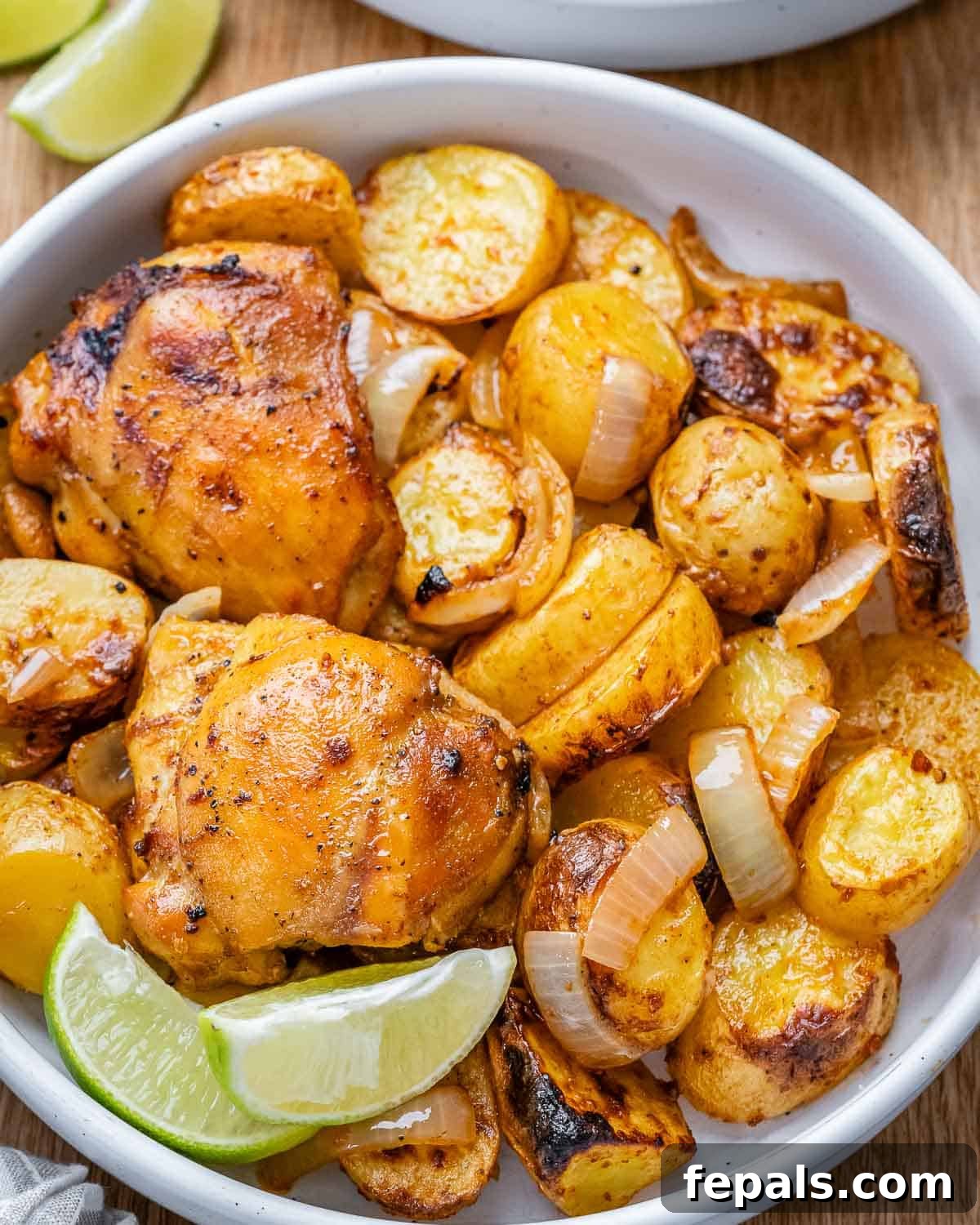 Close-up of crispy, golden potatoes and baked chicken thighs nestled together in a bowl, garnished with fresh herbs.