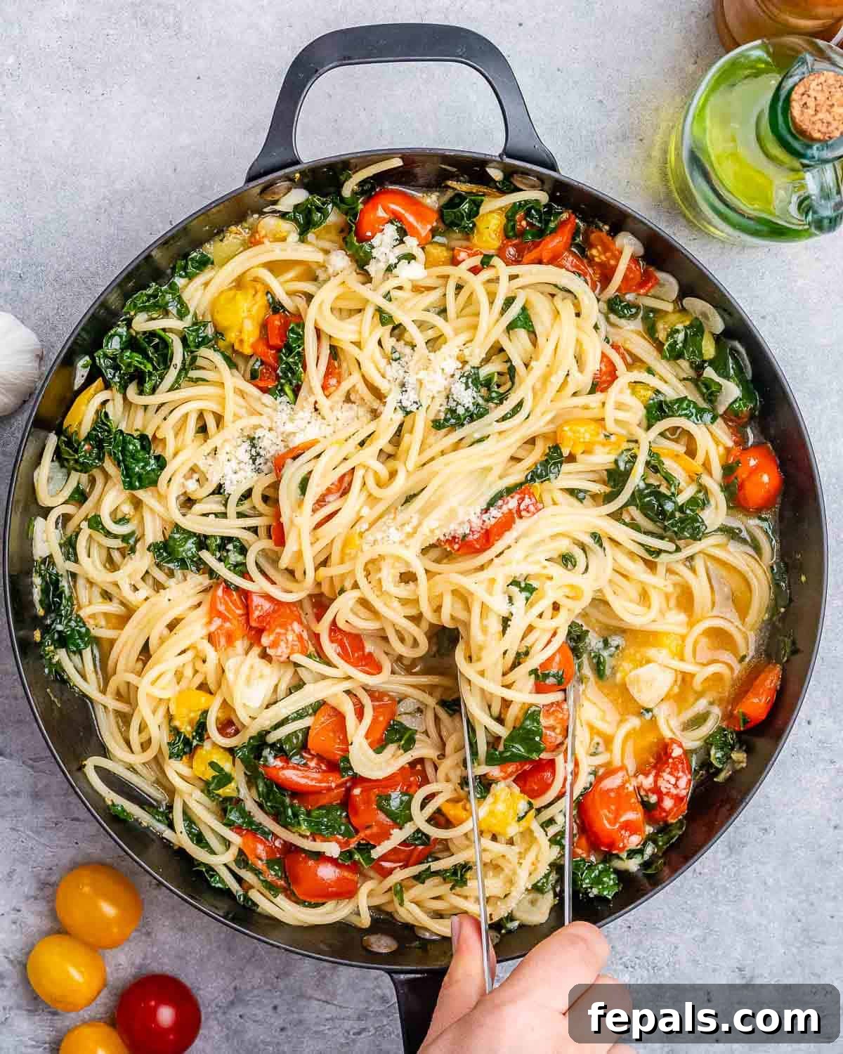 hand holding a skillet with spaghetti, tomatoes, and kale.