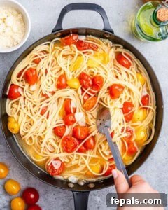 hand holding tongs and mixing the pasta and cherry tomatoes in a skillet.
