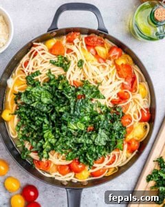 chopped kale added over cooked pasta in a skillet.