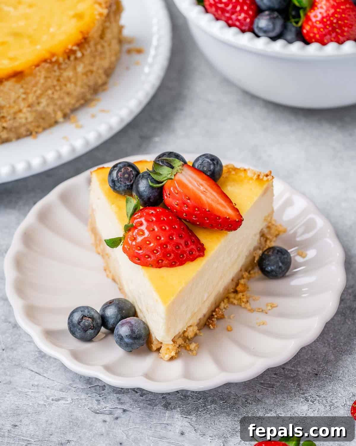 A beautifully plated slice of cottage cheese cheesecake on a scalloped edge plate, garnished with fresh blueberries and perfectly halved strawberries.