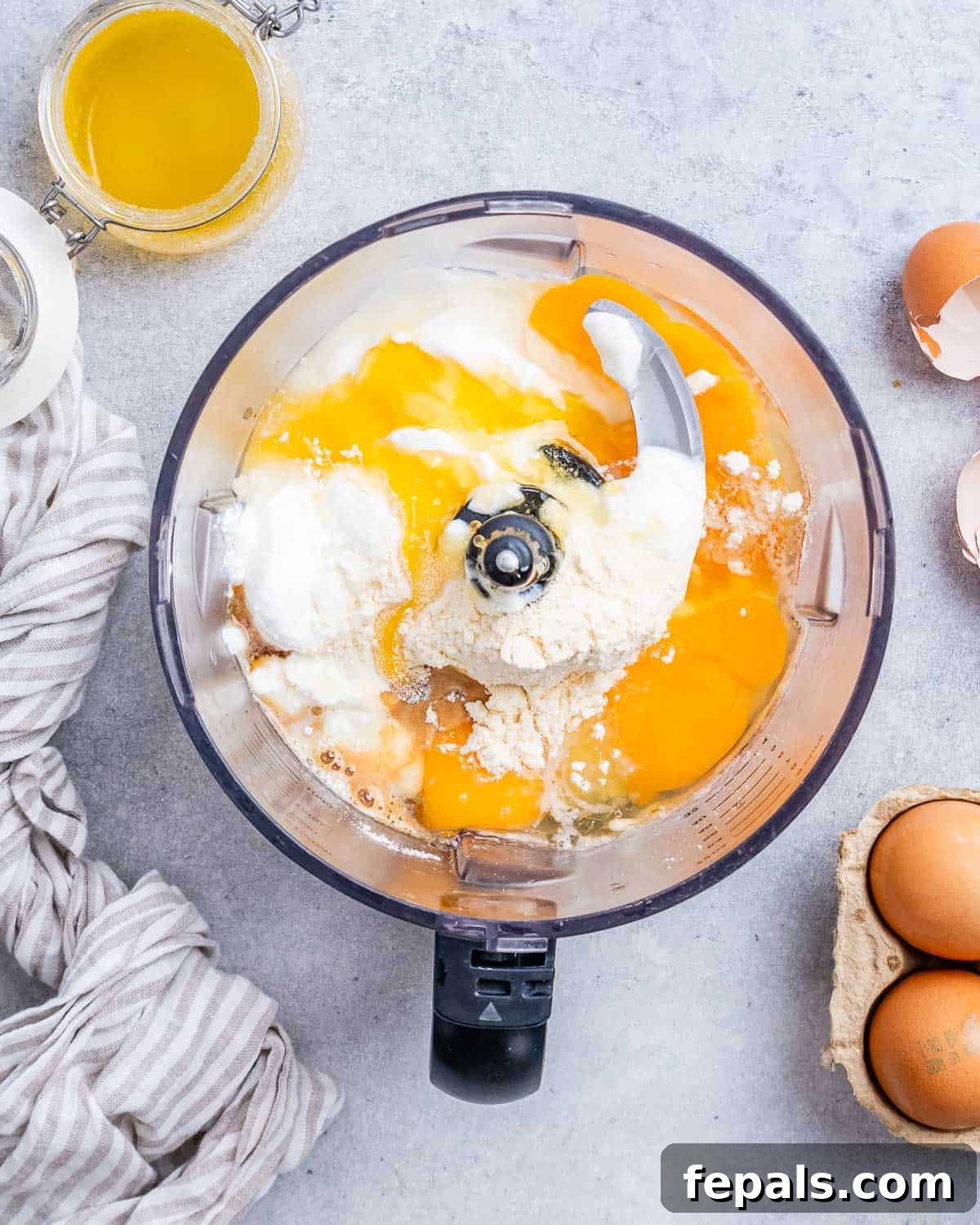 Food processor containing cottage cheese, eggs, honey, vanilla extract, and protein powder, ready to be blended into a smooth cheesecake filling.