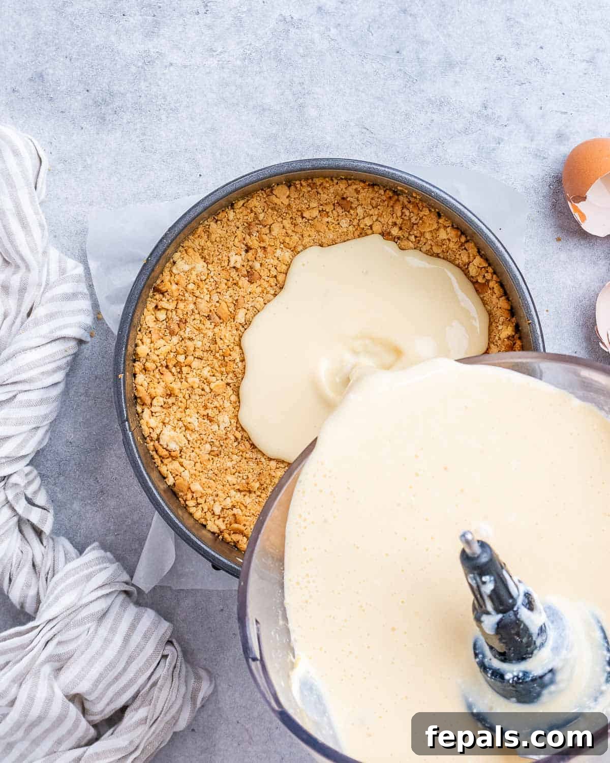 Smooth cheesecake filling being carefully poured over the baked graham cracker crust in a round baking pan, ready for its water bath.