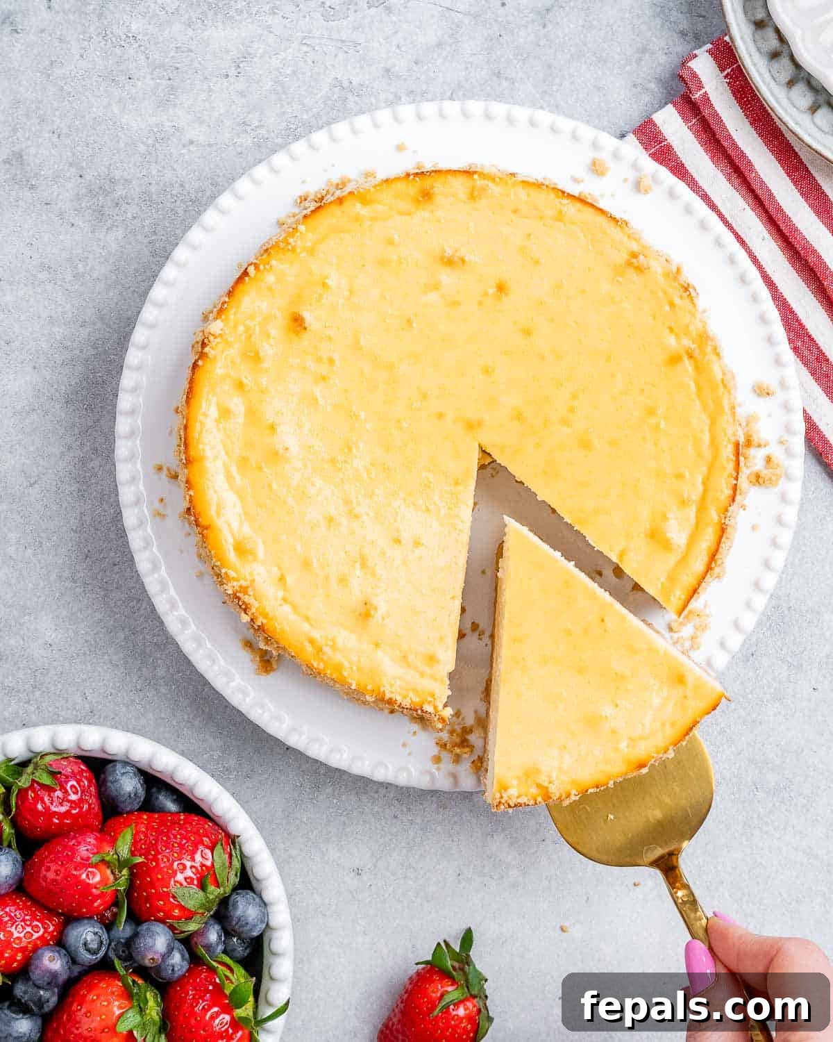 A whole baked cottage cheese cheesecake with one slice removed, adorned with fresh berries, highlighting its golden crust and creamy interior.
