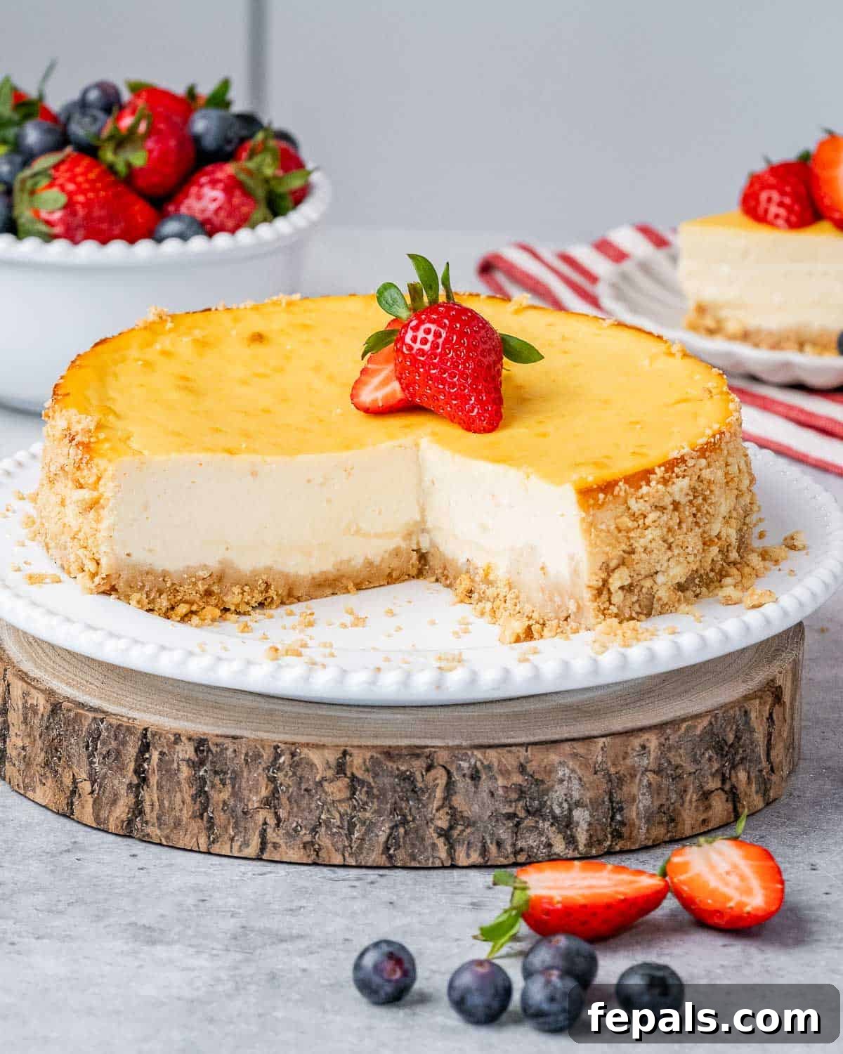 A beautifully presented whole cheesecake on a rustic wooden platter, generously topped with vibrant fresh strawberries, ready to be sliced and served.