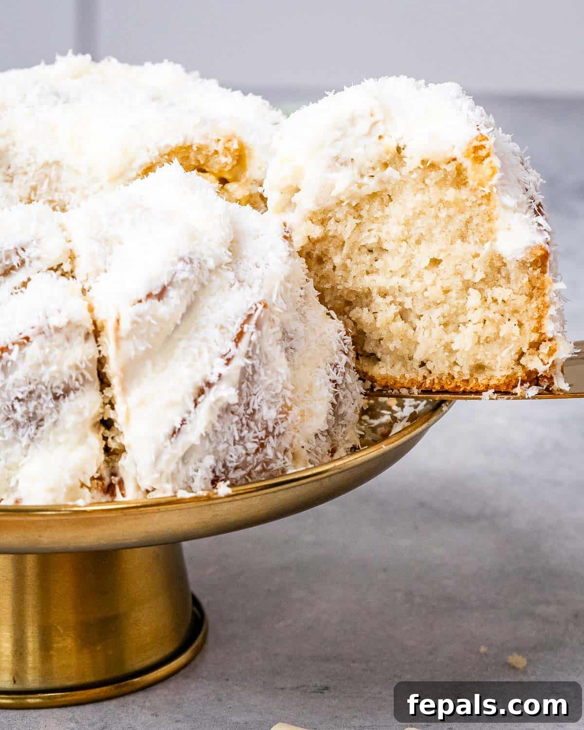 Tropical Coconut Bliss Cake 11 A close-up view of the complete coconut bundt cake, with several slices already removed, perfectly showcasing its soft, layered texture and the generous application of thick, creamy frosting adorned with delicate coconut flakes.