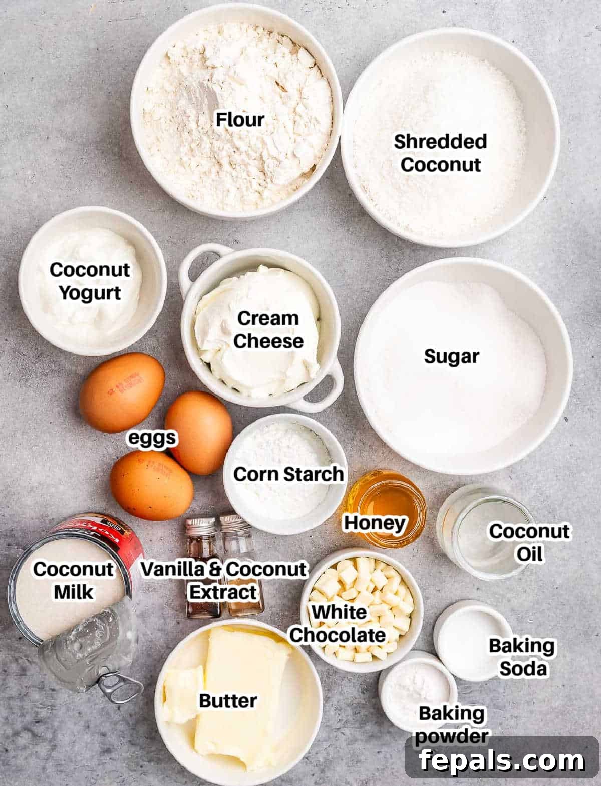 Tropical Coconut Bliss Cake 3 An overhead shot showcasing an array of labeled ingredients for coconut cake, including bags of flour and shredded coconut, fresh eggs, cans of coconut milk, a block of cream cheese, and white chocolate chips.