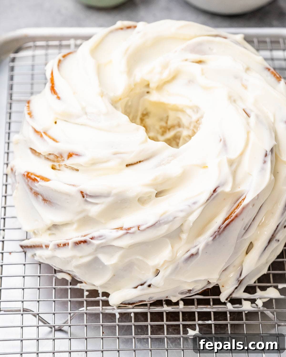 Tropical Coconut Bliss Cake 9 A beautifully frosted bundt cake cooling on a wire rack, adorned with elegant swirls of creamy coconut cream cheese frosting and generously topped with shredded coconut flakes, awaiting its final presentation.
