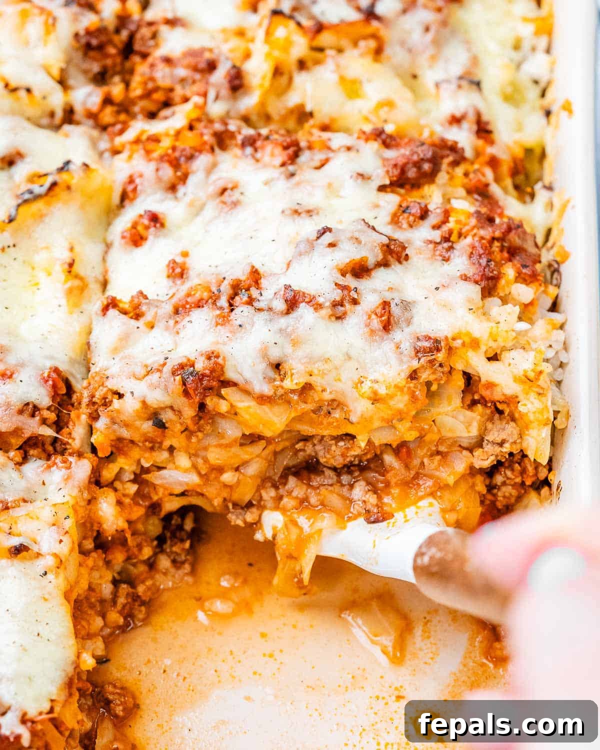 Easy Cabbage Roll Bake 2 A beautifully baked Cabbage Roll Casserole in a white ceramic baking dish, ready to be served, emitting steam and showcasing golden-brown melted mozzarella cheese on top, with layers of tender cabbage, seasoned ground beef, and rice visible beneath.