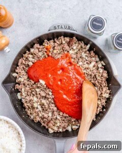 Easy Cabbage Roll Bake 11 Marinara sauce and beef broth being stirred into the browned ground beef and aromatics in a skillet, creating the rich casserole sauce.