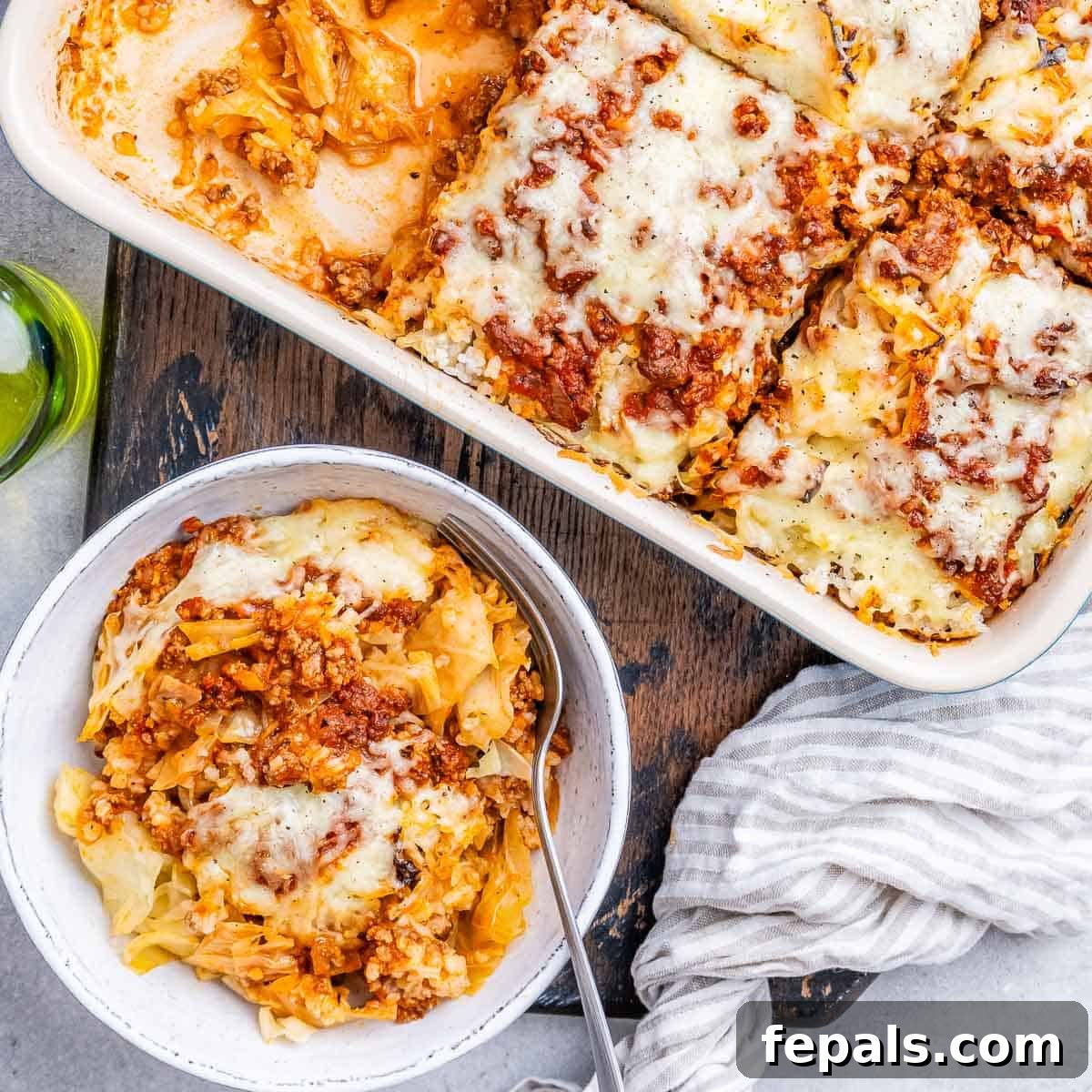 Easy Cabbage Roll Bake 15 A beautifully presented serving of Cabbage Roll Casserole in a white bowl, placed next to the full baking dish and a striped kitchen towel, ready to be enjoyed.