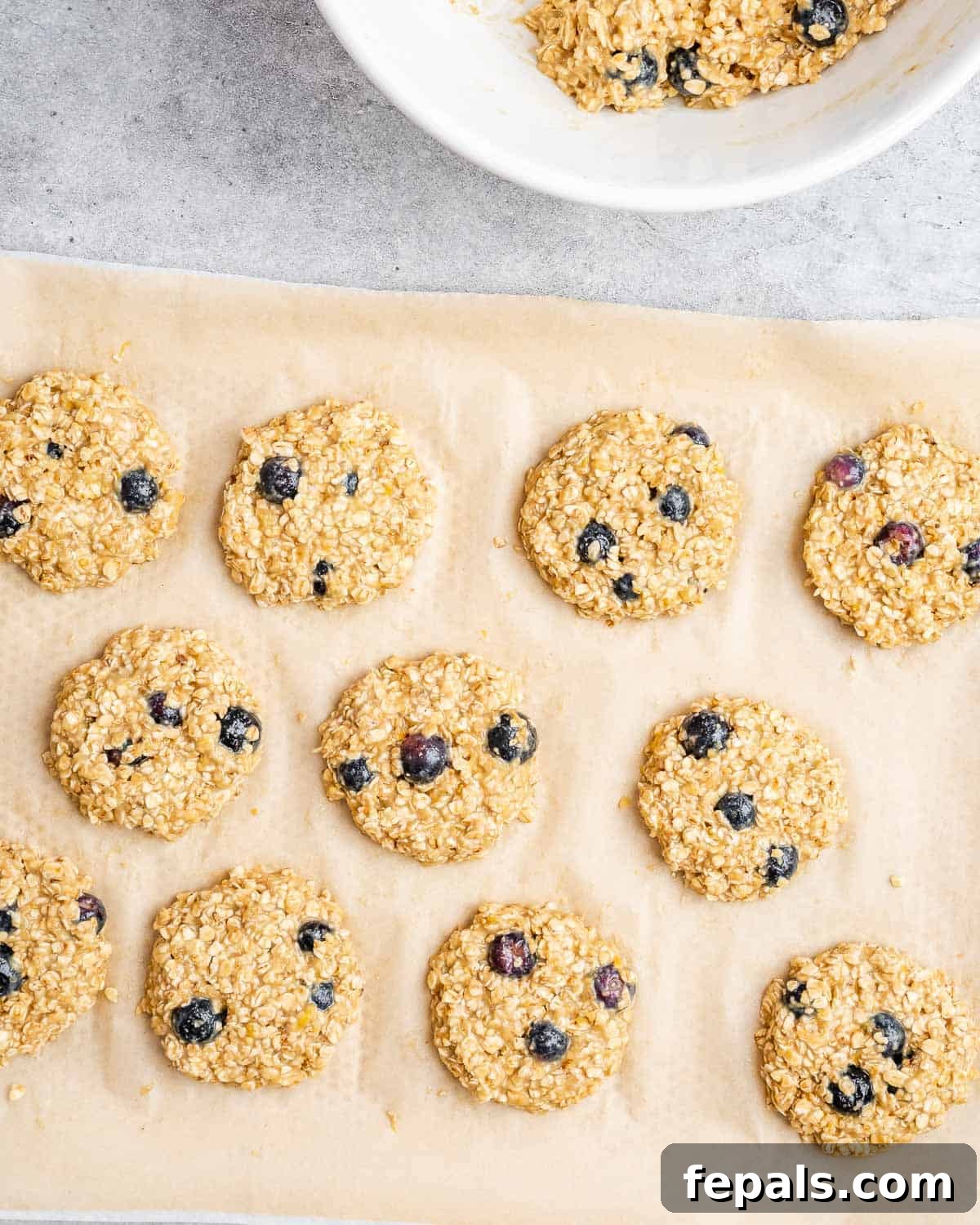 Soft-Baked Blueberry Oatmeal Cookies 8 Scoops of oatmeal cookie dough, with visible blueberries, neatly placed on a parchment-lined sheet pan before baking.
