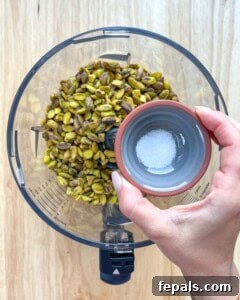 Pistachio and salt are being added to a food processor.