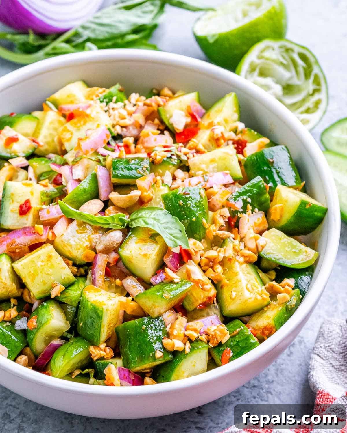 A white bowl with vibrant Thai Cucumber Salad, garnished with fresh herbs and peanuts.