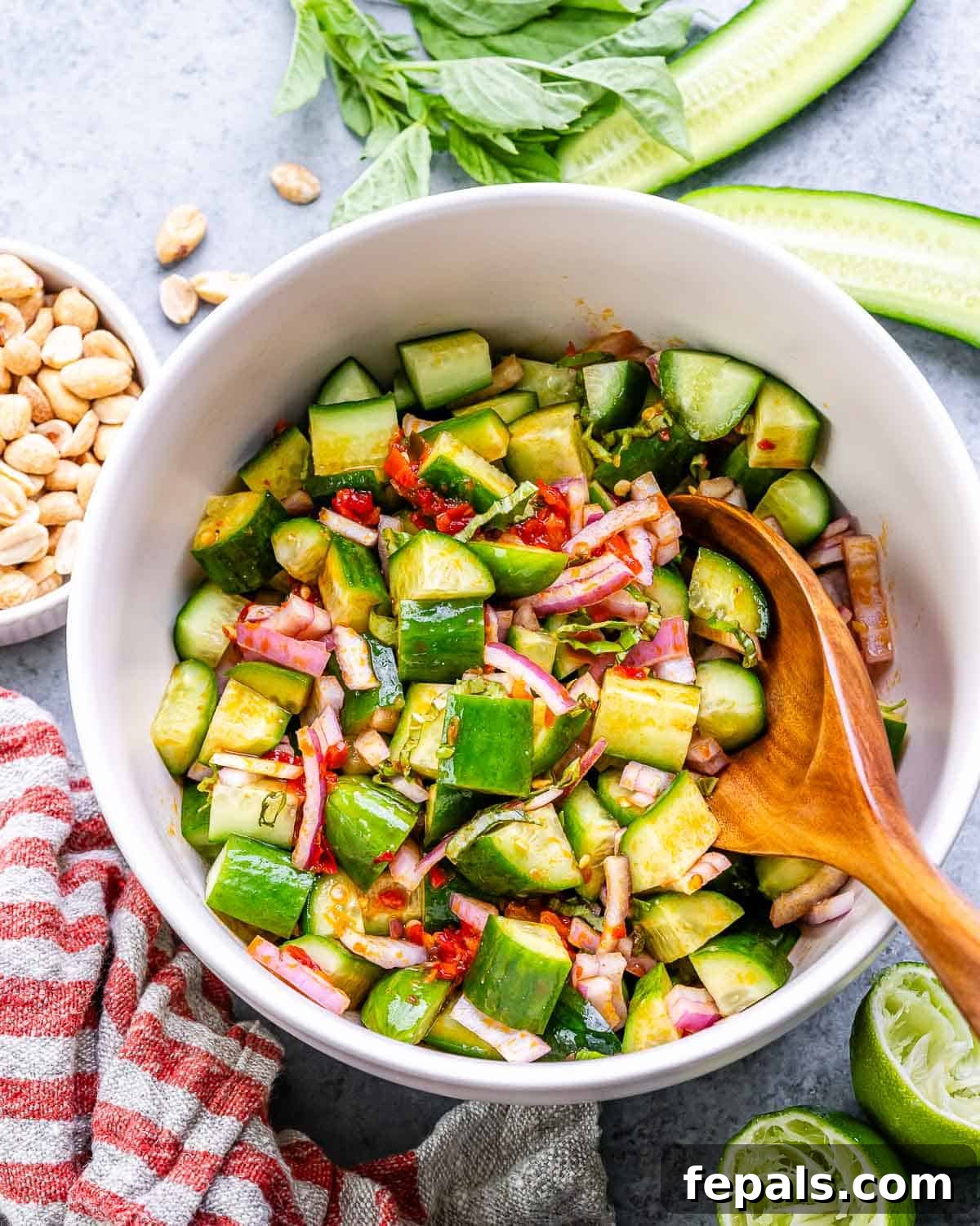 Asian cucumber salad in a white bowl with a wooden serving spoon, highlighting the freshness and texture.