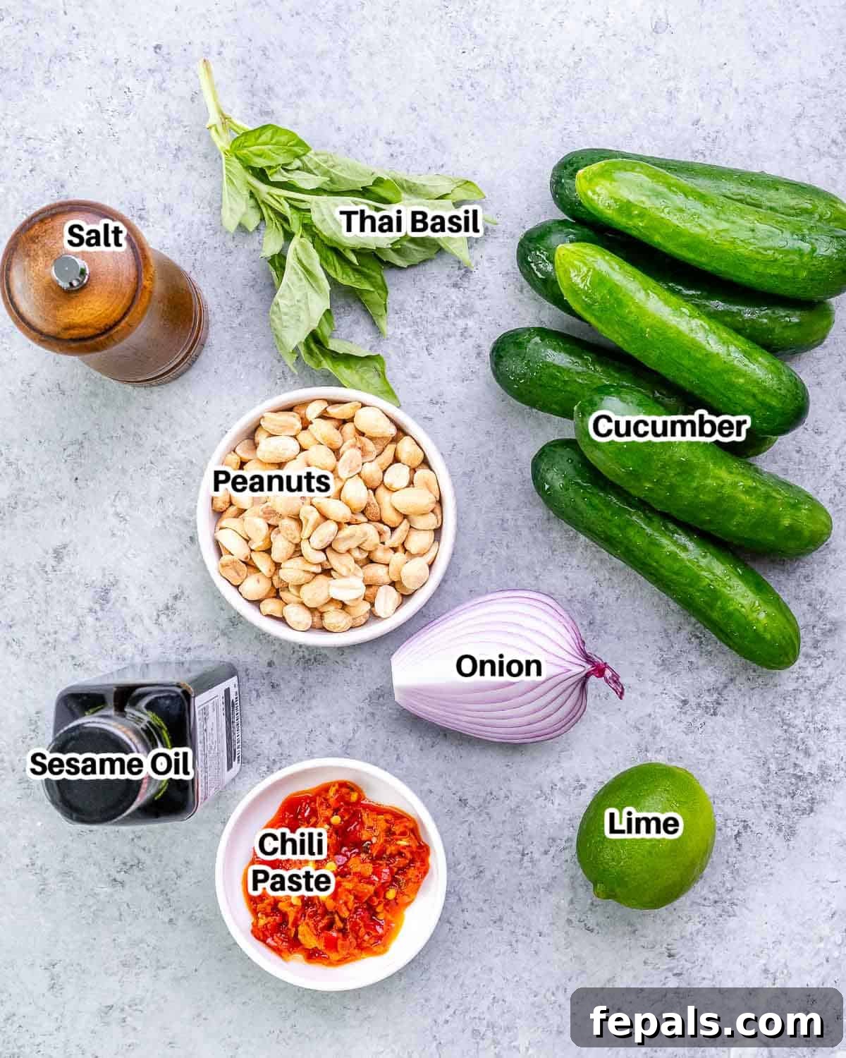 A flat lay of fresh ingredients laid out to make Thai cucumber salad, including cucumbers, red onion, basil, chili paste, and lime.