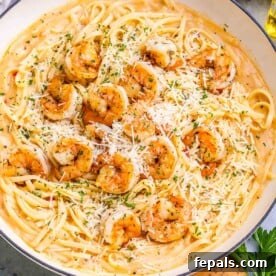 A pan with creamy pasta topped with cooked shrimp and sprinkled with cheese.