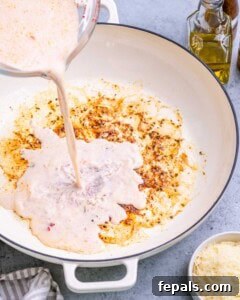 Pouring almond milk mixture into a skillet with sautéed garlic and oil.