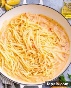 Cooked linguine added to the creamy sauce in the skillet.
