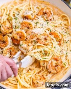 Tongs lifting a shrimp from the pasta to show detail and texture.