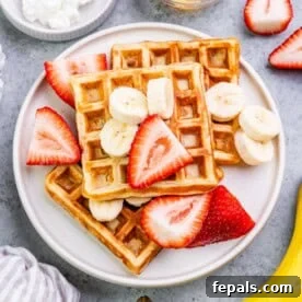 waffles on a plate topped with slices of strawberries ans bananas.