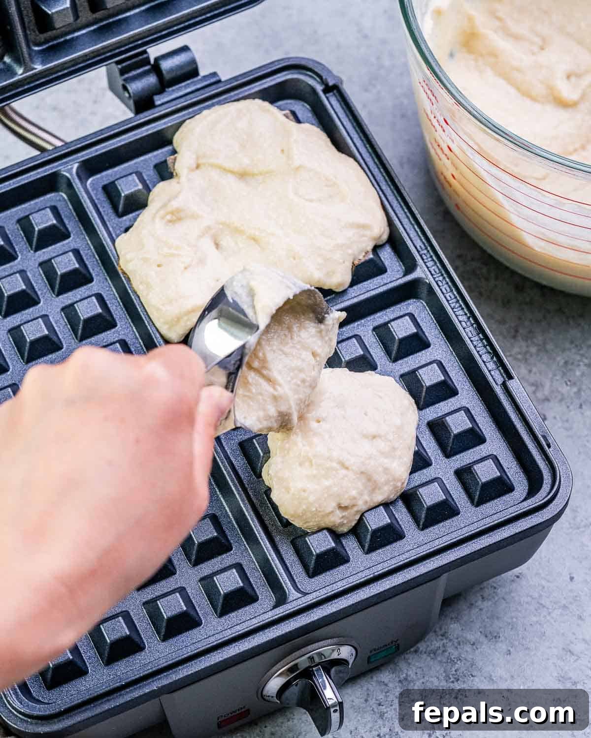 Smooth waffle batter is being carefully poured onto a preheated waffle maker, filling the grids evenly.