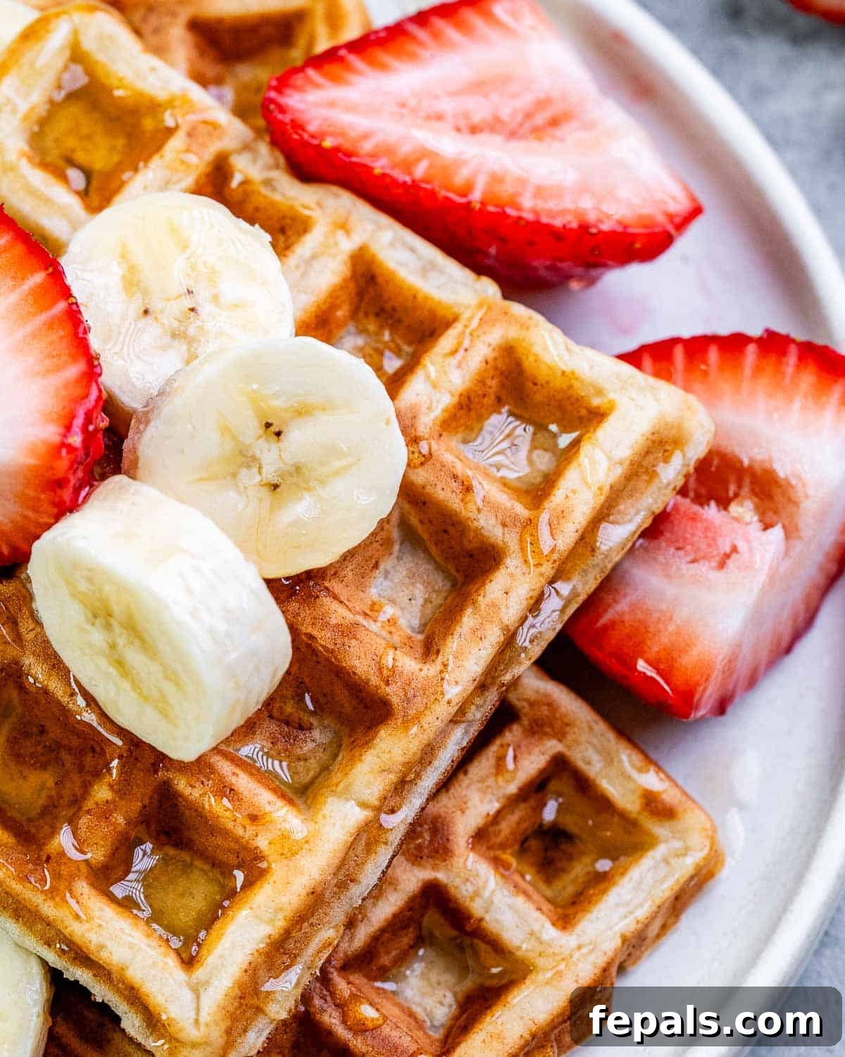 A stack of golden cottage cheese waffles on a white plate, beautifully garnished with an assortment of fresh berries like strawberries, blueberries, and raspberries.