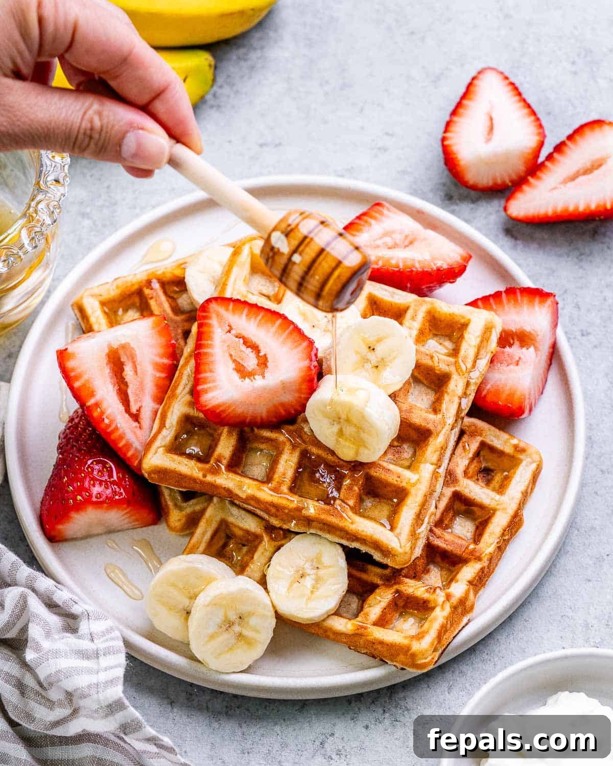 A stream of golden honey gracefully drizzles over a freshly cooked cottage cheese waffle, highlighting its textured surface and golden-brown perfection.