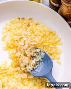Homestyle Cottage Cheese Lasagna 8 Sautéing diced onions and minced garlic in olive oil in a white pan, creating the aromatic base for the lasagna's tomato sauce.