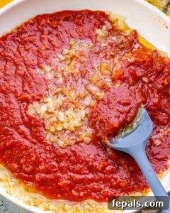 Homestyle Cottage Cheese Lasagna 9 Adding a jar of rich marinara sauce to sautéed onions and garlic in a pan, preparing the flavorful tomato sauce layer for the lasagna.