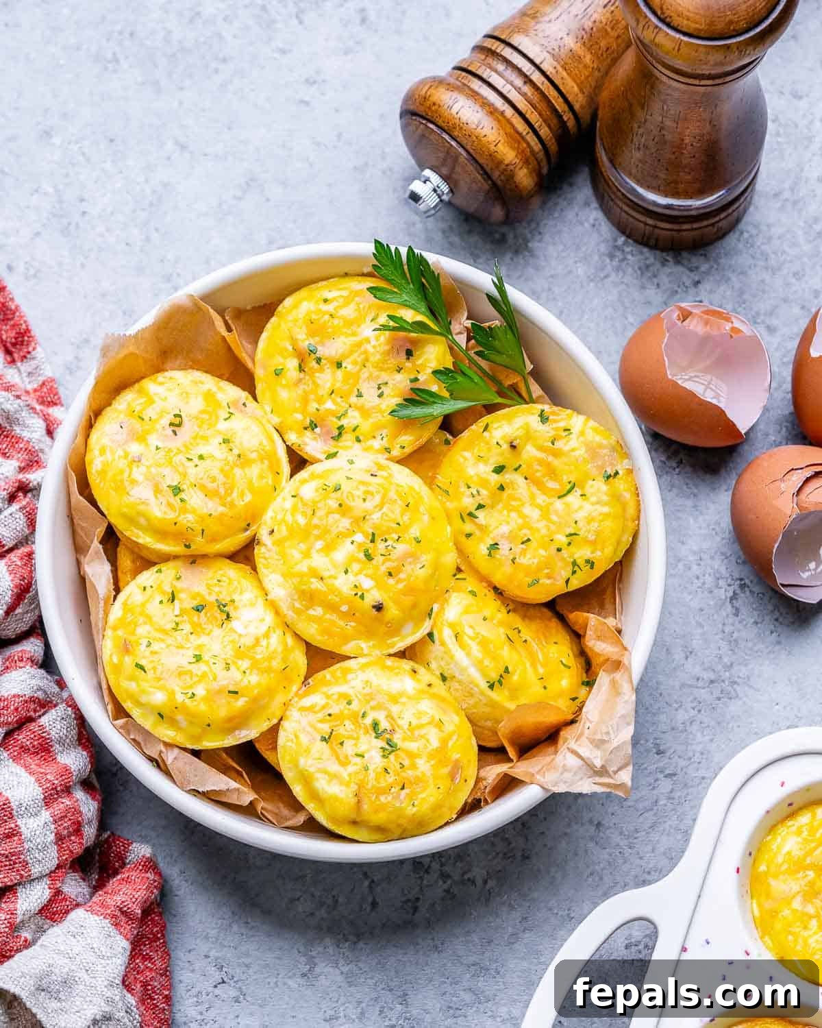 Protein-Packed Cottage Cheese Egg Cups 7 An overhead shot of cottage cheese egg bites in a white bowl, with eggshells scattered on the table, emphasizing the fresh ingredients.