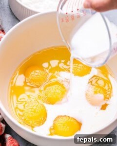 Process shot showing eggs being whisked with milk and cottage cheese in a large measuring jug.