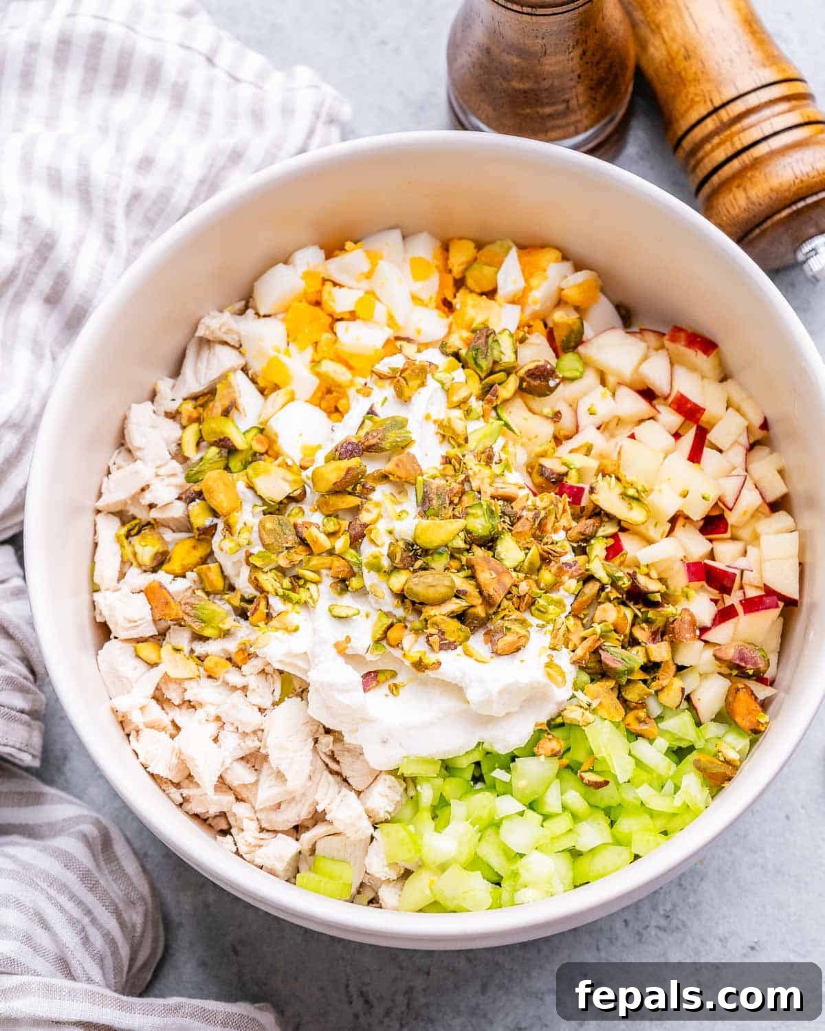 Light and Creamy Cottage Chicken Salad 6 Diced celery, apples, hard-boiled eggs, and chopped pistachios arranged over the chopped chicken in a white mixing bowl.
