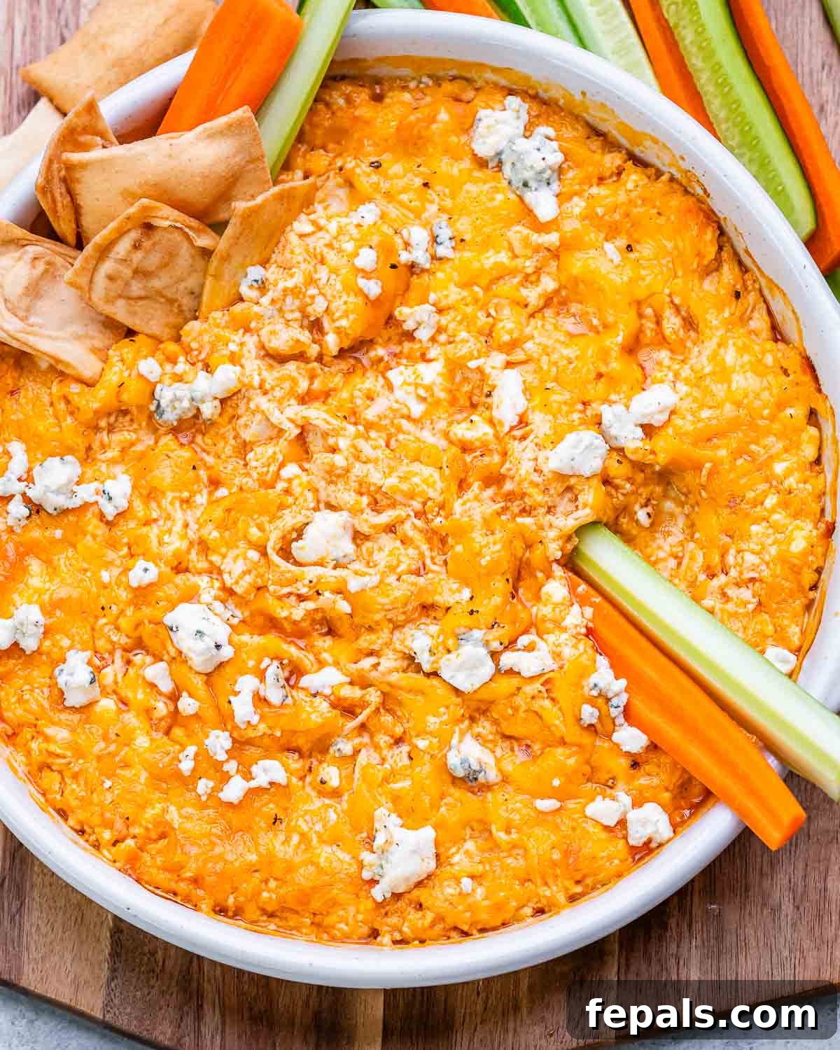 A white baking dish filled with freshly baked cottage cheese buffalo chicken dip, garnished with crumbled blue cheese and fresh parsley, served with crisp celery and carrot sticks on the side.