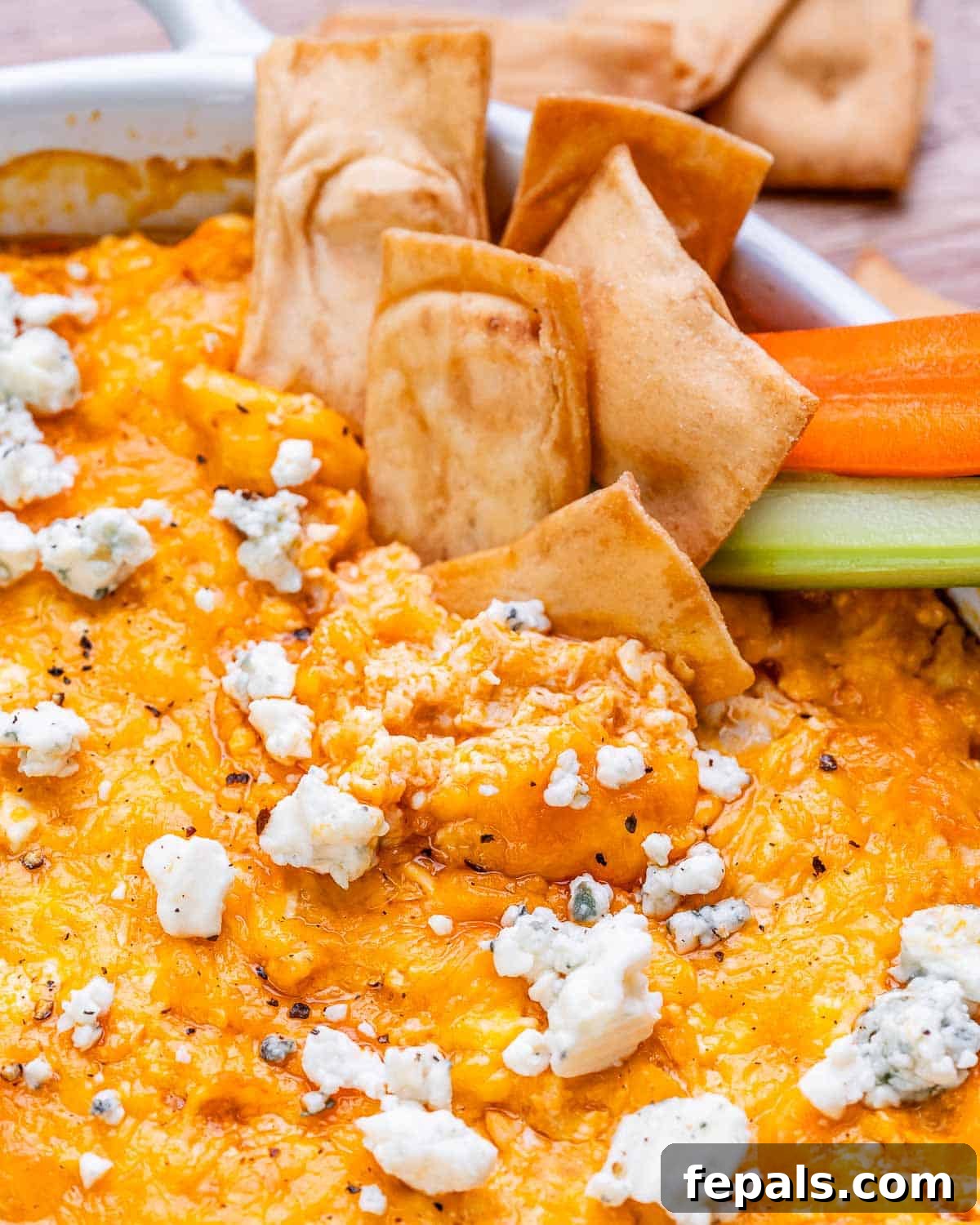 A scoop of creamy cottage cheese buffalo chicken dip being lifted with a pita chip, surrounded by fresh celery and carrot sticks on a serving platter.