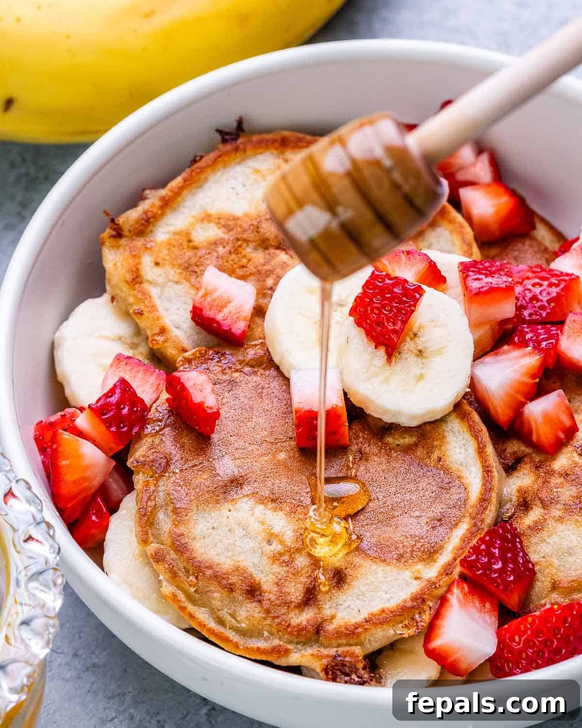 Drizzling honey on cottage cheese pancakes with sliced banana and strawberry