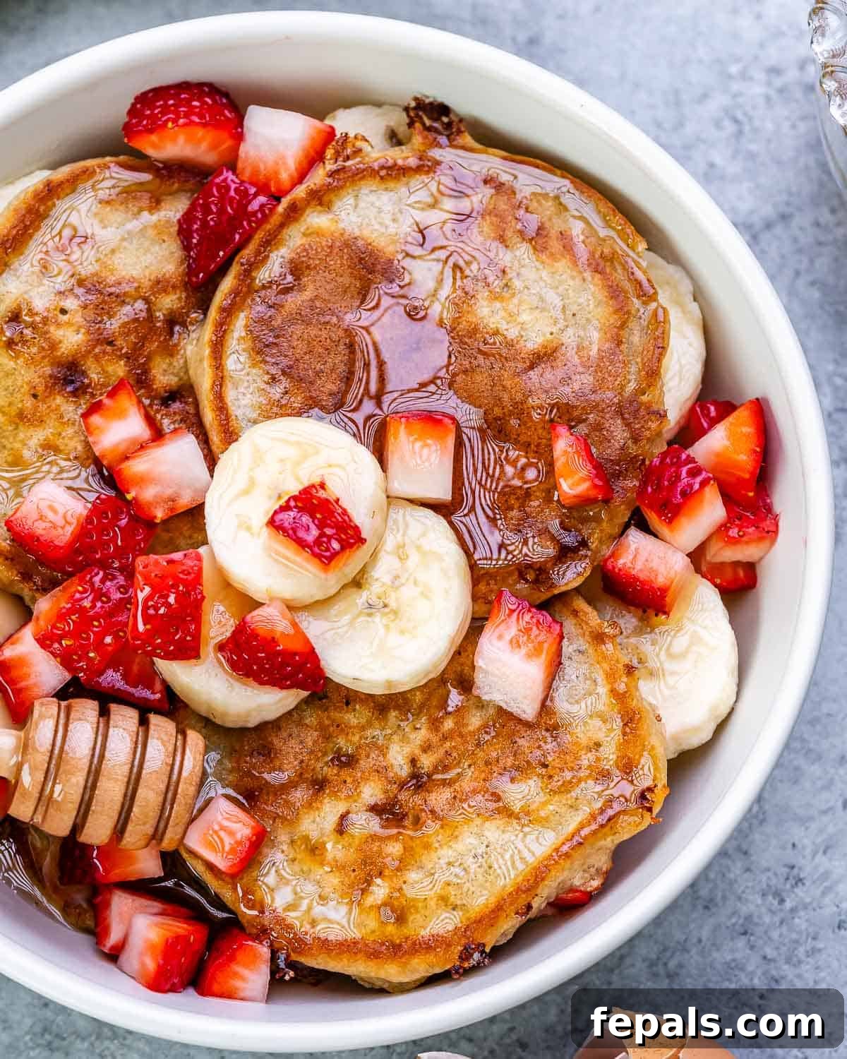 A bowl of fluffy banana cottage cheese pancakes garnished with fresh strawberries and banana slices.