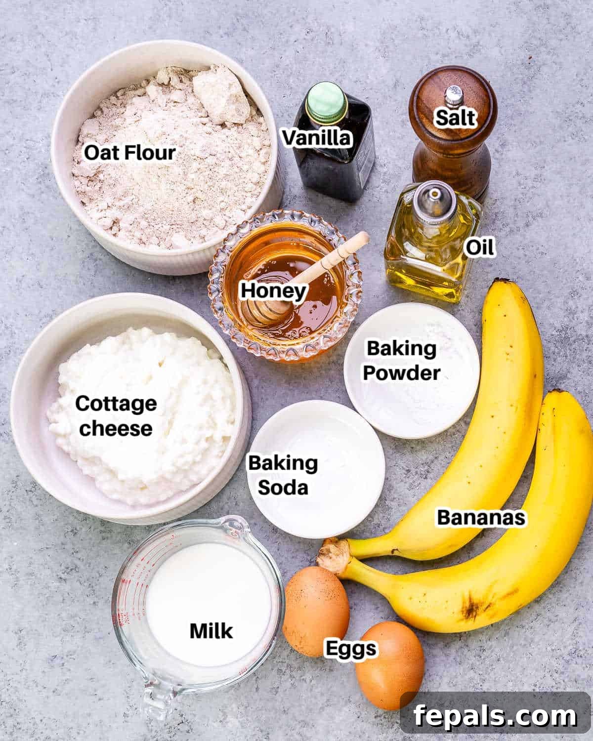 Arrangement of fresh ingredients including eggs, cottage cheese, bananas, honey, milk, vanilla extract, and oat flour, ready for making pancakes.