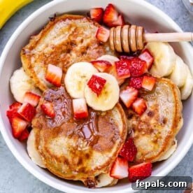 pancakes in a bowl topped with sliced bananas and chopped strawberries.