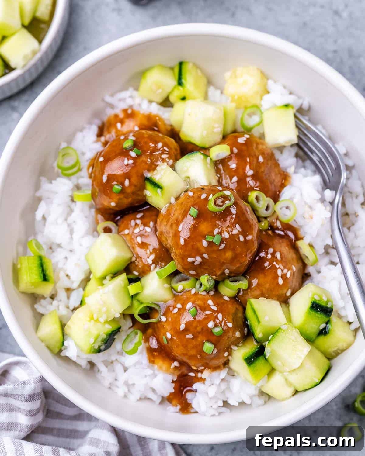 Sticky Teriyaki Turkey Meatballs 2 Meatballs over rice, topped with chopped cucumber and sesame seeds.