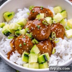 Sticky teriyaki meatballs over rice, garnished with green onions and sesame seeds.