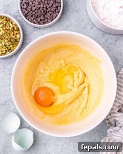 A mixing bowl with the creamed butter and sugar mixture, and one cracked egg added on top, ready to be mixed in.